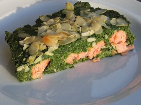 Saftiges Lachsfilet in cremigem Spinat-Auflauf, überbacken mit goldbraunen gehobelten Mandeln, auf weißem Teller angerichtet im warmen Licht