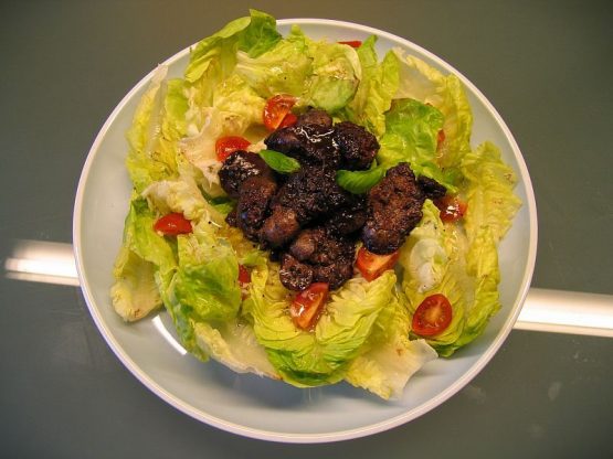 Gebratene Hähnchenleber in dunkler Rotweinreduktion auf grünem Blattsalat mit Kirschtomaten und frischem Basilikum, angerichtet auf weißem Teller