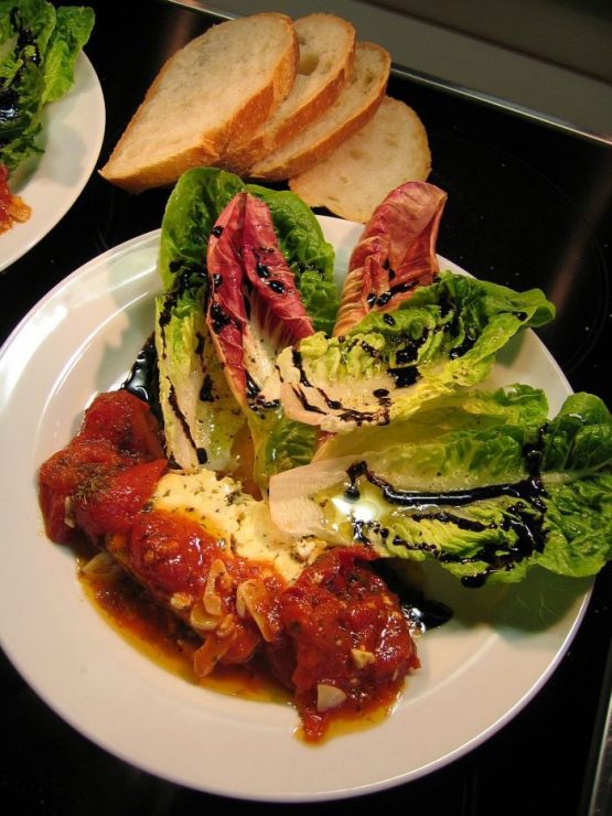 Gemischter Salat mit gebackenem Schafkäse, geschmolzenem Feta in Tomatensauce, Romana-Salat, Parmesan und Crema di Balsamico auf weißem Teller angerichtet