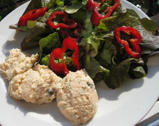 Lachscreme neben Blattsalat mit roten Paprikaringen auf einem weißen Teller