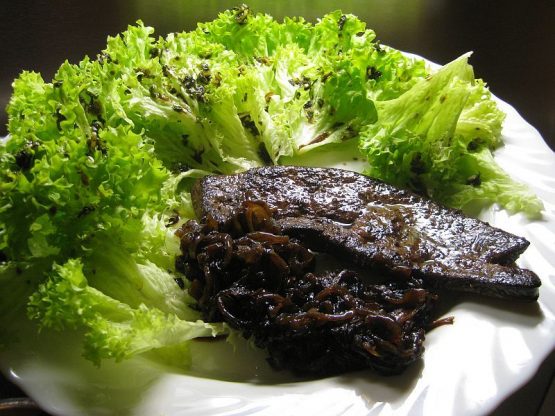 Gebratene Rinderleber mit dunklen Balsamicozwiebeln und grünem Blattsalat auf weißem Teller angerichtet