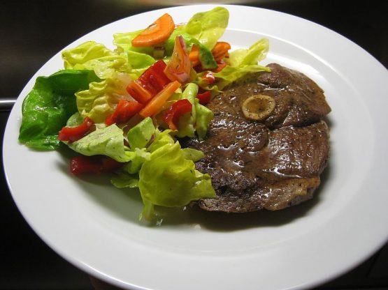 Gebratene Scheibe vom Lamm mit Knoblauch-Sahne-Sauce, serviert mit frischem Blattsalat, Paprika und Gurke auf weißem Teller