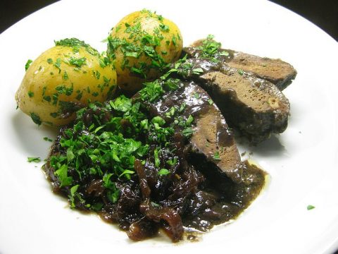 Gebratene Schweineleber mit Zwiebeln in dunkler Porterbier-Sauce, dazu junge Kartoffeln und gehackte Petersilie auf weißem Teller angerichtet.