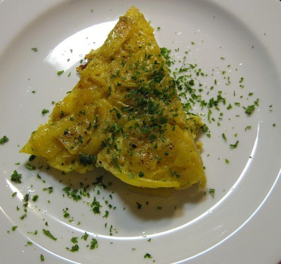 Goldgelbes Kartoffelomelett mit dünnen Kartoffelscheiben und Zwiebeln, aufgeschnitten auf weißem Teller, mit Petersilie bestreut, leicht gebräunt und saftig im Inneren