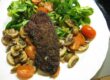 Gebratene Kalbsleber mit Madeira Sauce auf Feldsalat, geschmorten Champignons und Cocktailtomaten auf weißem Teller.