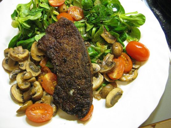 Gebratene Kalbsleber mit Madeira Sauce auf Feldsalat, geschmorten Champignons und Cocktailtomaten auf weißem Teller.