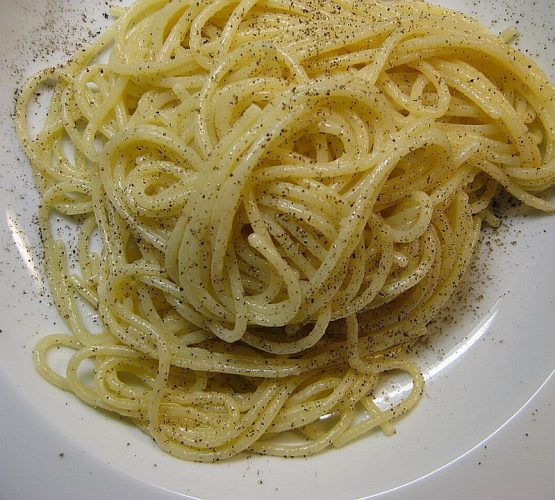 Spaghetti mit Traubenkernöl und schwarzem Trüffelaroma auf einem weißen Teller mit frisch gemahlenem Pfeffer.