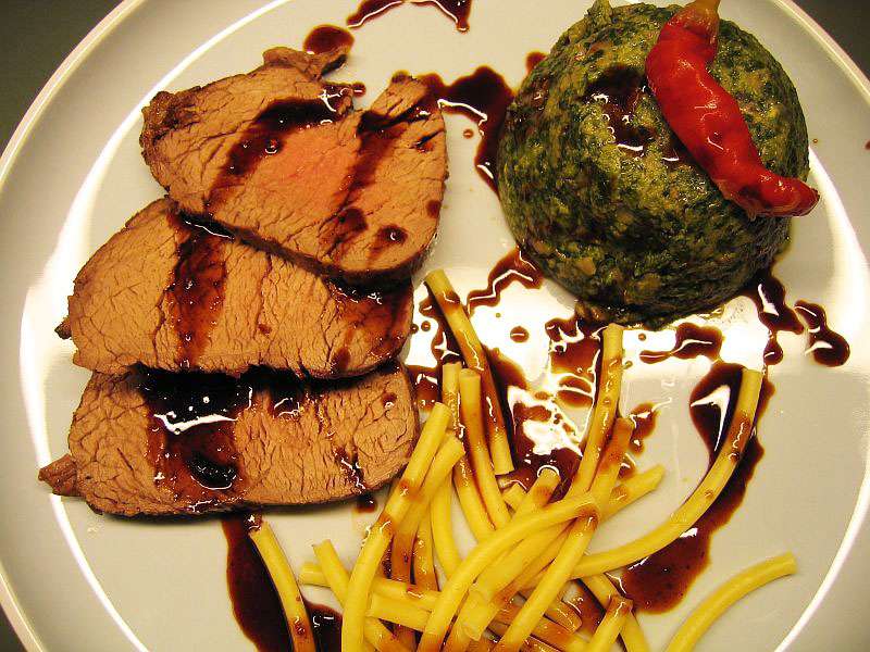 rindslende-vom-charolaisrind-mit-madeirasauce-und-spinat-im-formchen In Scheiben geschnittenes Charolais Rinderfilet mit dunkler Madeirasauce, dazu gestürzter Spinat im Förmchen und einfache Nudeln auf hellem Teller angerichtet.