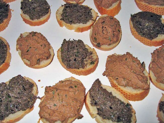 Geröstete Crostini mit toskanischer Hühnerlebercreme und schwarzer Olivenpaste auf einer Servierplatte.
