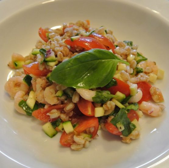 Getreidesalat umbrische Art mit Dinkel, Tomaten, Zucchini, Basilikum und Nordseekrabben auf einem weißen Teller angerichtet.