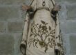 Holzskulptur der Maria zürnt mit Krone und weit ausgebreiteten Armen in einer steinernen Kirchenwand, Blick leicht erhoben, Gewand mit floralen Mustern verziert