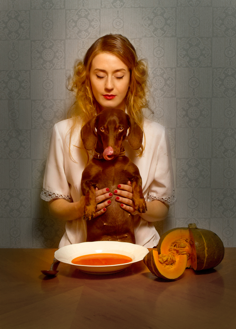 Die Fotografie Horst Kistner Tischgebet zeigt eine Frau mit Dackel in der Hand vor einem Suppentopf