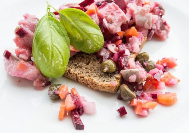 Dank der Tiefkühlung kann Matjessalat mit Roter Bete das gesamte Jahr über zubereitet werden. In den Niederlanden ist wegen irgendwelcher - nicht näher zu beschreibenden - Dinge eine Tiefkühlung vor der Verarbeitung von 40 Grad im Minus vorgeschrieben. Also hat sich die früher übliche Saison der Matjes deutlich verändert. Es wird für diesen der Hering zwischen Mai und Juni genommen. Dieser ist sehr fett, weil er noch keinen Stress mit der Fortpflanzung hat und weder Milch noch Rogen gebildet hat. Der Matjes wird für ungefähr 5 Tage in Salzlake eingelegt, wobei die Enzyme der im Fisch belassenen Bauchspeicheldrüse den Fisch fermentieren. Das ohnehin schon gut zu verdauende, wertvolle Fett wird noch bekömmlicher. Es gibt 1000 Arten einen Fischsalat zu bereiten. Matjessalat mit Roter Bete ist aber farblich sicher einer der attraktivsten. Und übrigens auch einer der Würzigsten wenn Sie ihn so ähnlich zubereiten, wie ich es getan habe. Es wird eine weiße Zwiebel in kleine Würfel geschnitten. Eine rohe Rote Bete Knolle wird mit dem Gemüseschäler geschält. Danach schneiden Sie bis fast an den Boden der Rübe sehr eng parallel einmal längs und einmal quer. Danach drehen sie die Rote Bete Rübe auf die Seite und schneiden sehr feine Scheiben. Siehe da schon sind kleine Würfel da. Zusätzlich schneiden sie noch kleine Möhren oder auch Karotten in winzige Würfelchen, so dass auch diese gut durchziehen können.Ich habe noch einige Sardellen gehackt und Kapern bereitgelegt. Sie Vermischen die Zutaten mit dem in kleine Stücke geschnittenen Matjes und geben einige Löffel Distelöl und einen satten Schluck Milch dazu. Matjessalat mit Roter Bete und Möhren sollte im Kühlschrank abgedeckt noch zwei Stunden Ziehen. Ein geröstetes Roggenbrot schmeckt hervorragend dazu.