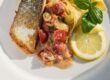 Gebratener Lachs mit knuspriger Haut, Bandnudeln und Krabbensoße mit Tomaten und Frühlingszwiebeln, dazu Basilikum und eine Zitronenscheibe.