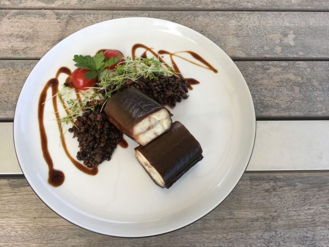 Belugalinsen mit geräuchertem Aal auf einem weißen Teller auf einem Holztisch