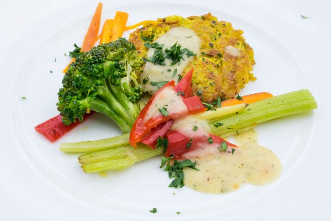 Hirsebratlinge Mit Gemüse und Soße auf einem Teller