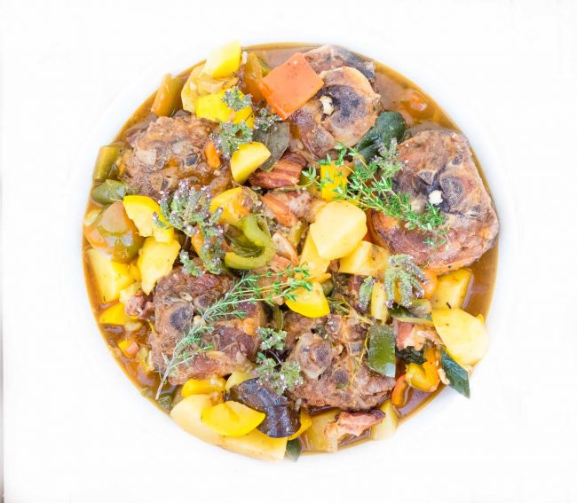 Ein Geschmorter Lammnacken mit Gemüse und Kräuterblüten auf dem Teller hübsch garniert.