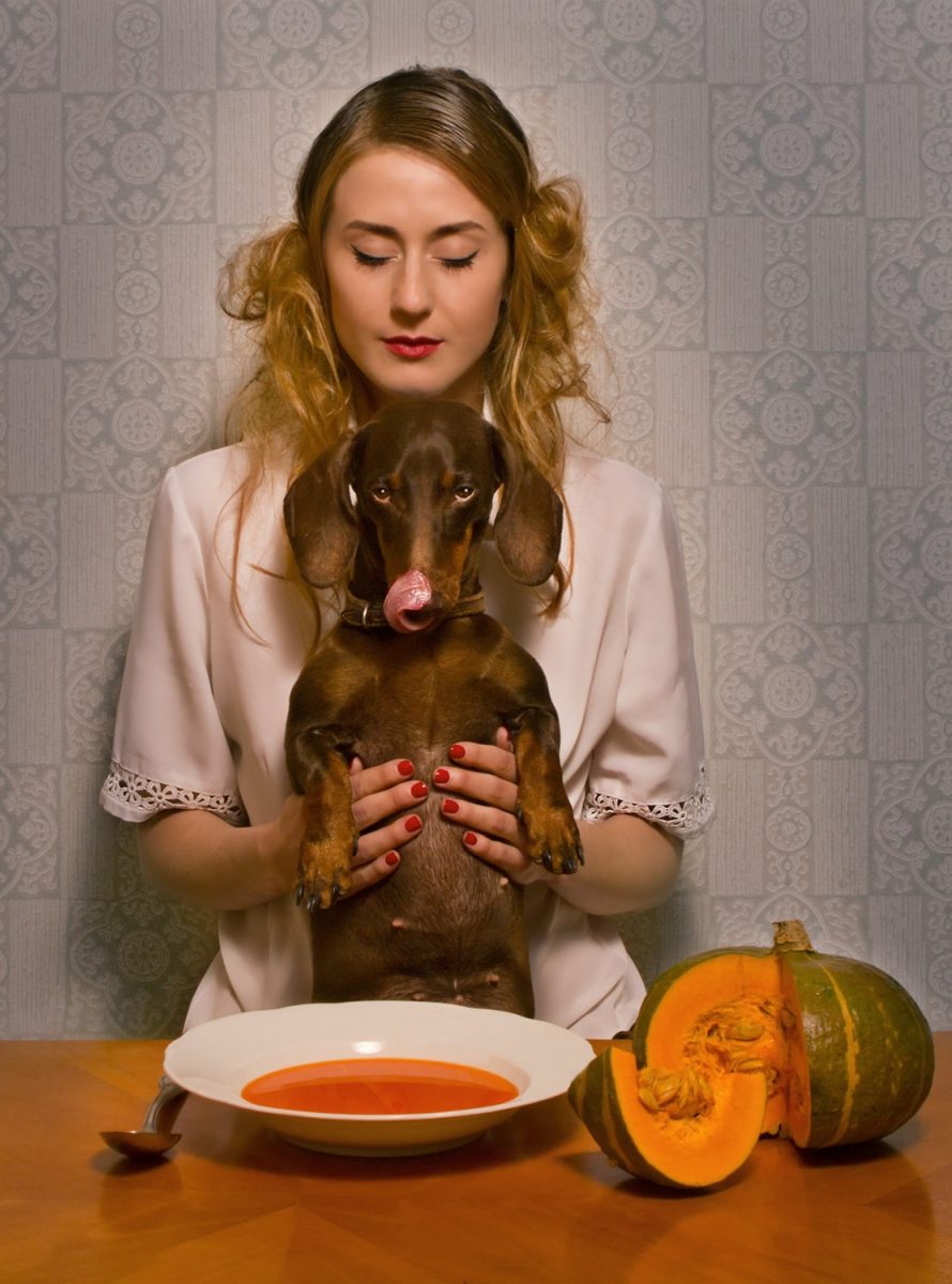 Die einzigartige Fotografie von Horst mit dem Titel Tischgebet zeigt eine junge Frau mit einem Dackel auf dem Schoß, der aus einem Teller Suppe nascht.