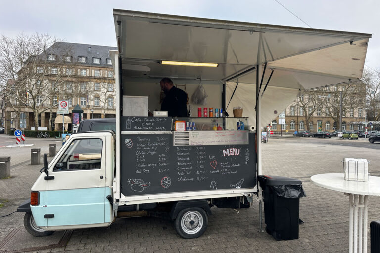 Ein skurriler Wurstwagen auf dem Karlsruher Bahnhofsvorplatz rettet diese gepflasterte Wüste zwar nicht, gibt ihr jedoch ein wenig Leben. Auf einem italienischen Piaggo einen Wurststand zu montieren ist genial.