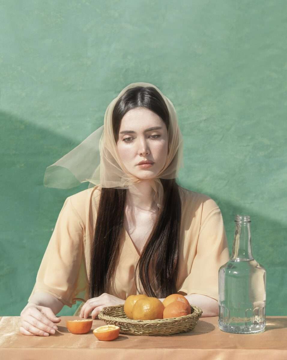 Das Werk Summer noon von Somy Samani ist ein Beispiel für visuelle Poesie unter der Last einer Realität, die vielen Frauen im Iran vertraut ist. Das Bild zeigt eine melancholische Frau, die vor einem Korb mit Orangen sitzt. Sie trägt ein zartes Kopftuch und scheint nachzudenken.