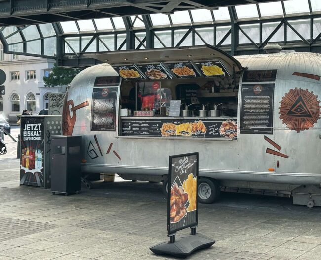 Der Foodtruck von dem Hamburger Hauptbahnhof ist ein amerikanisches Modell und hat Stil. Bei diesem bekommt man eine gute Currywurst in der Tüte.