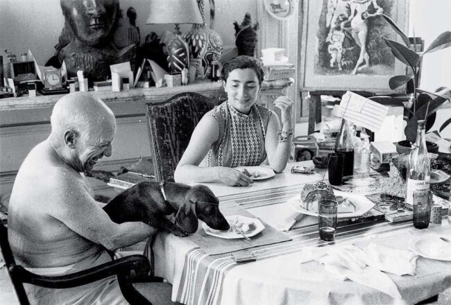 Picasso, Jacqueline Roque, und der Dackel Lump. 1957 gemeinsam beim Essen. Pablo Picasso liebte Tiere – besonders Hunde. Mit Menschen hatte er oft Probleme.
