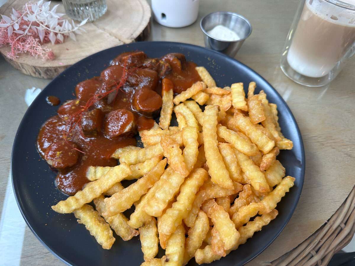 Teller mit Currywurst und Pommes im Bistro Werk Bad Laasphe, serviert mit hausgemachter Sauce und Dip.