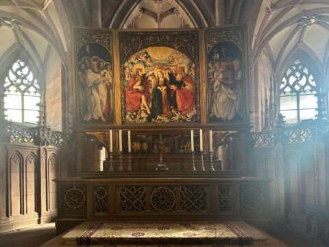 Hochaltar von Hans Baldung Grien im Freiburger Münster mit geöffneter Schauseite und der Darstellung der Marienkrönung in der Mitteltafel. Lichtdurchfluteter Kirchenraum mit gotischem Maßwerk.