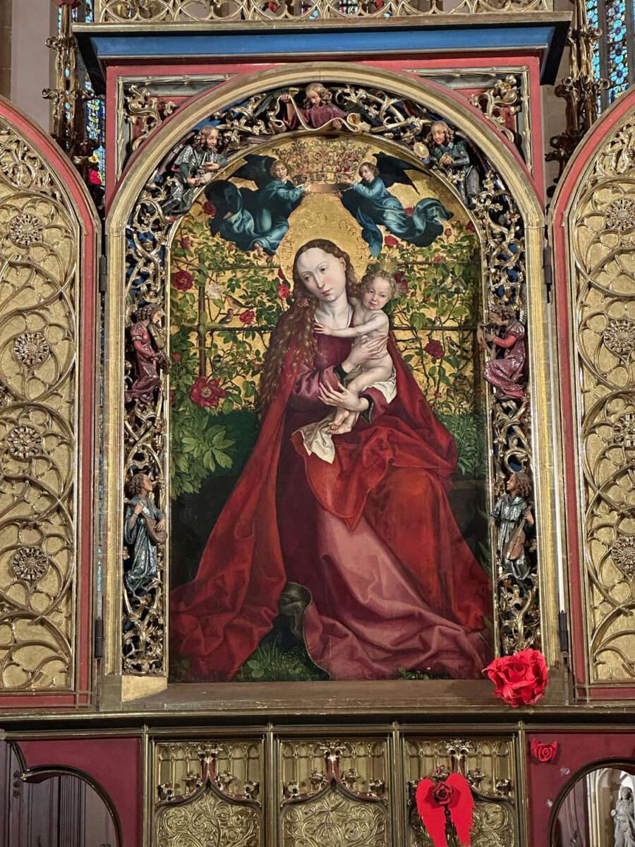 Madonna im Rosenhag von Martin Schongauer – spätmittelalterliches Altarbild in der Dominikanerkirche Colmar, mit infantilen roten Papierblümchen verziert.