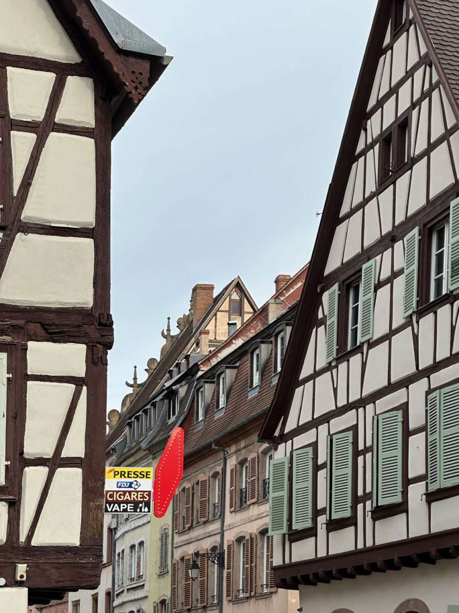 Enge Altstadtgasse in Colmar mit hohen Fachwerkhäusern, grünen Fensterläden und einem traditionellen Tabac-Presse-Ladenschild für Zeitungen und Tabakwaren.