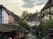 Kanal der Petite Venise in Colmar mit dicht stehenden Fachwerk- und Wohnhäusern, Restauranttischen am Wasser, Schwänen auf dem Kanal und ruhiger Altstadtatmosphäre.