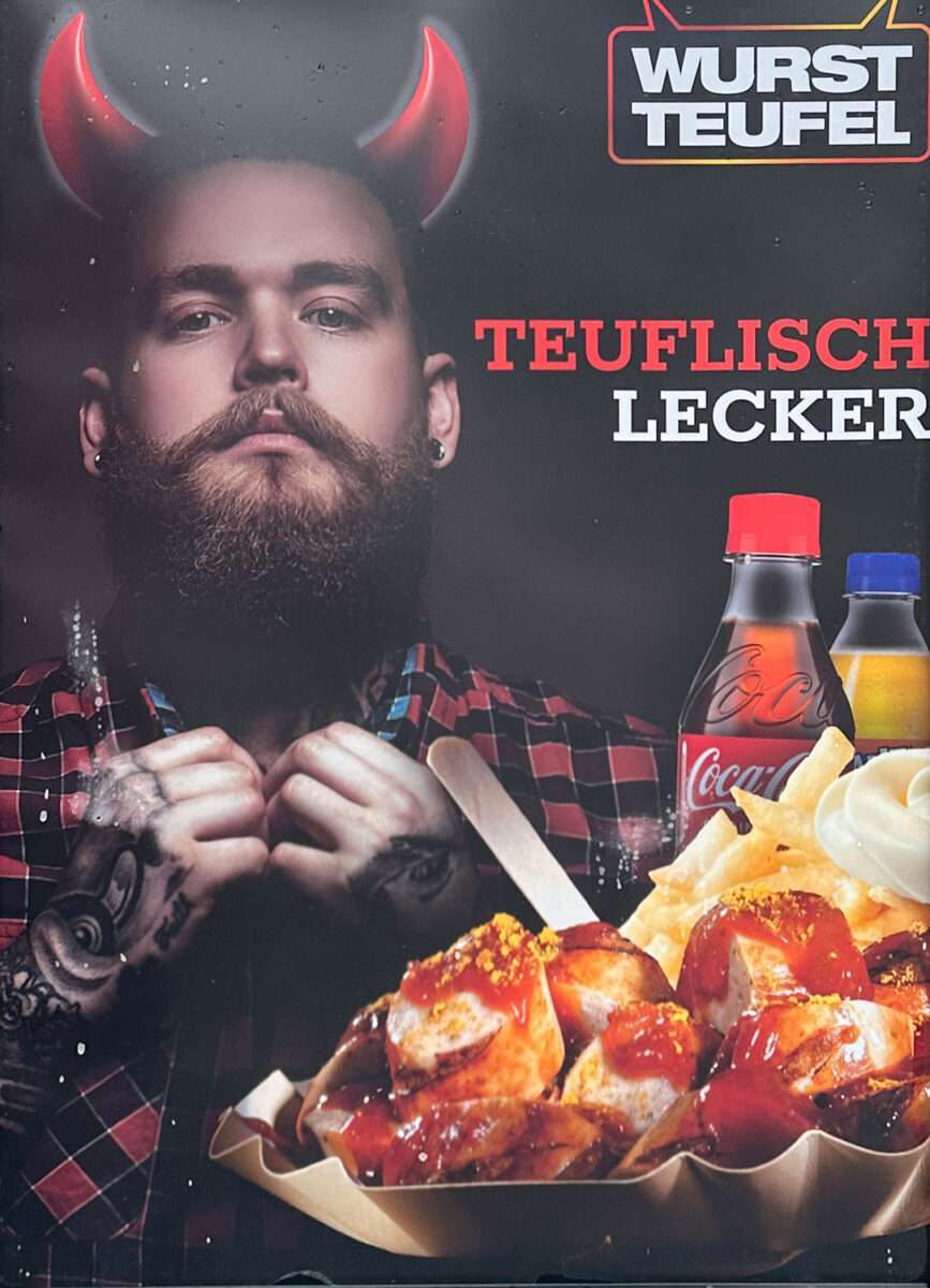 wurstteufel-werbeplakat-teuflisch-lecker Werbeplakat mit bärtigem Mann mit Teufelshörnern und Currywurst mit Pommes unter dem Schriftzug „Teuflisch lecker“ und Logo Wurstteufel.
