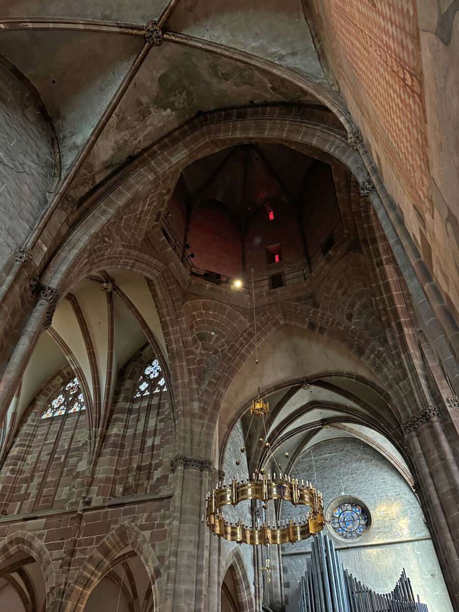 Blick nach oben in Gewölbe und Turmraum der Kirche St. Peter und Paul in Wissembourg mit Steinarchitektur und hängendem Kronleuchter