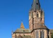 Kirche St. Peter und Paul in Wissembourg mit hohem gotischem Turm aus rotem Sandstein über den Dächern der Stadt unter blauem Himmel