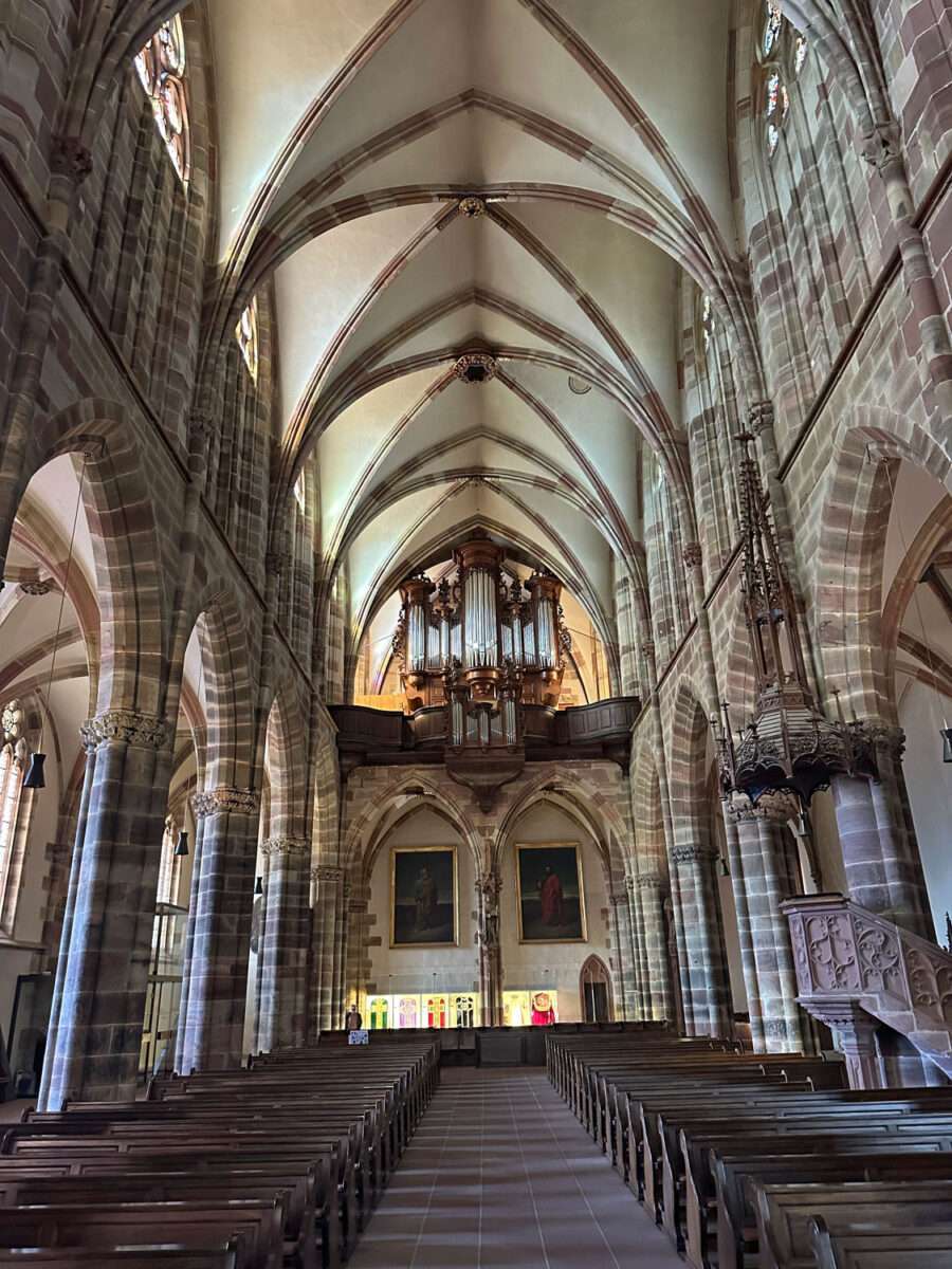 Mittelschiff der Kirche St. Peter und Paul in Wissembourg mit Sitzreihen, gotischen Pfeilern und Orgel auf der Empore