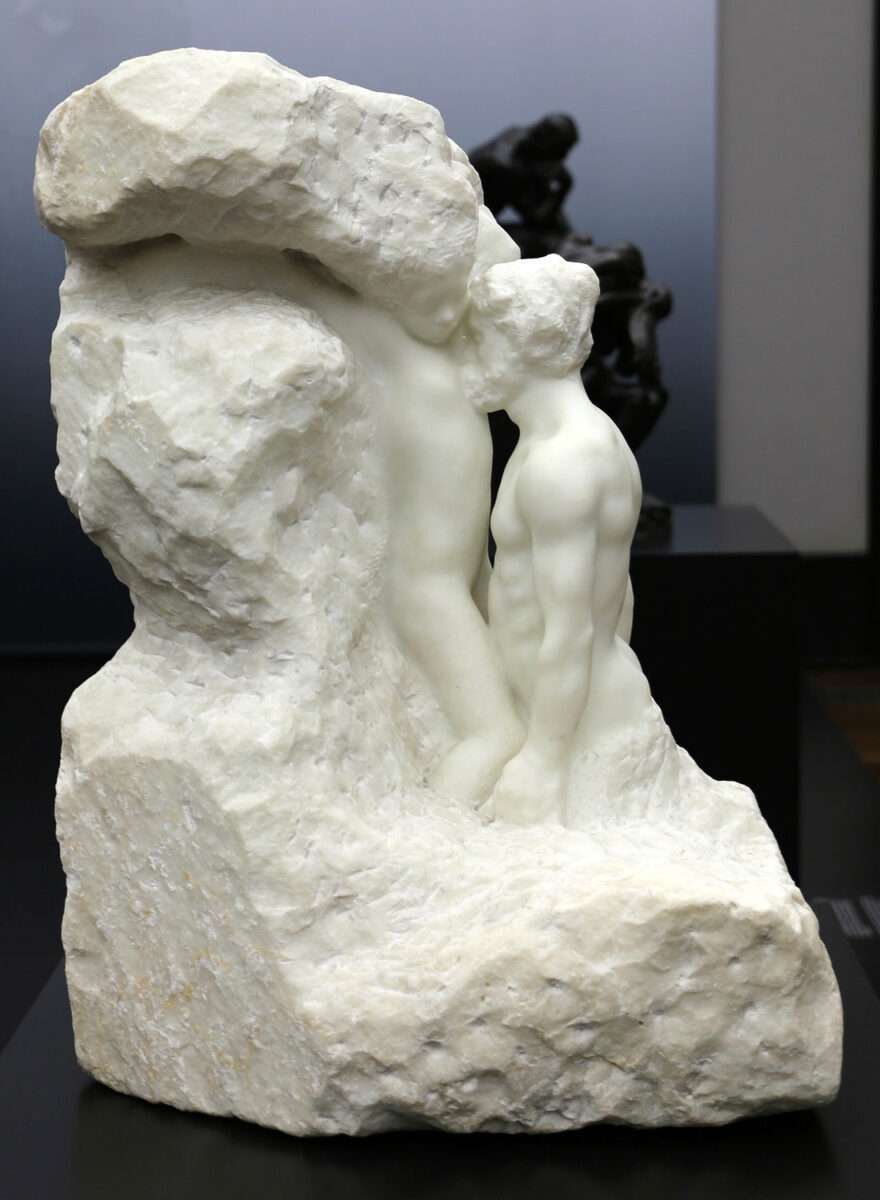 Zwei nackte Figuren sind eng ineinander verschlungen; eine Figur beugt sich über die andere, deren Körper halb liegend auf einem rohen Steinblock ruht, die Oberfläche bleibt teilweise unbearbeitet.