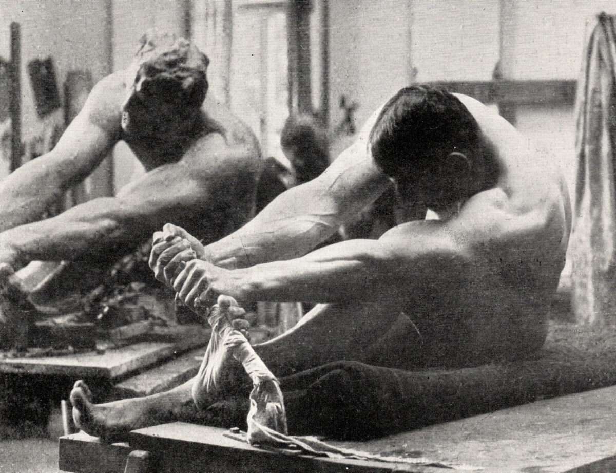 Historische Schwarzweißaufnahme eines männlichen Aktmodells im Atelier von Max Klinger, das eine gespannte Sitzhaltung einnimmt und einen Ast umfasst, Vorstudie zur Dramagruppe.