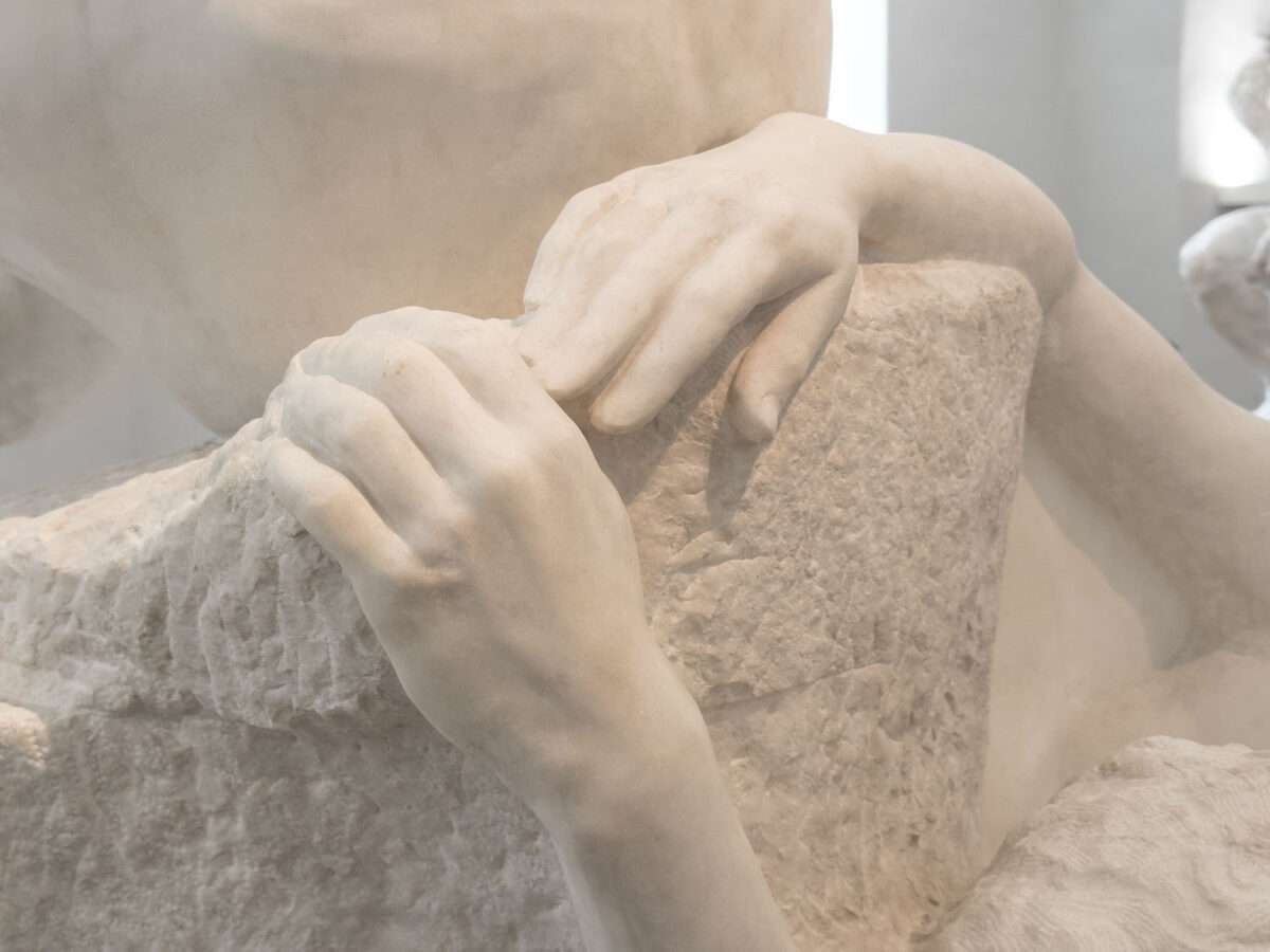 Detail zweier Hände, die sich an einer rauen Steinfläche festhalten, Teil der Dramagruppe von Max Klinger im Albertinum Dresden, glatte Haut kontrastiert mit unbearbeitetem Stein.