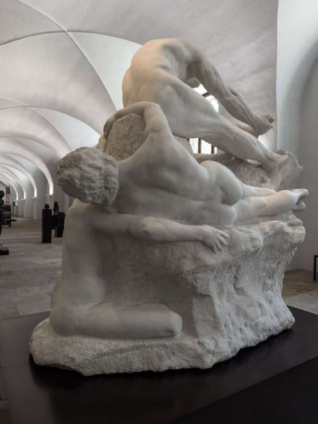 Rückansicht der Dramagruppe mit liegender weiblicher Figur, kauernder Figur und nach vorne gebeugtem Athleten, alle teilweise mit dem Steinblock verbunden, im Albertinum Dresden unter gewölbter Decke.