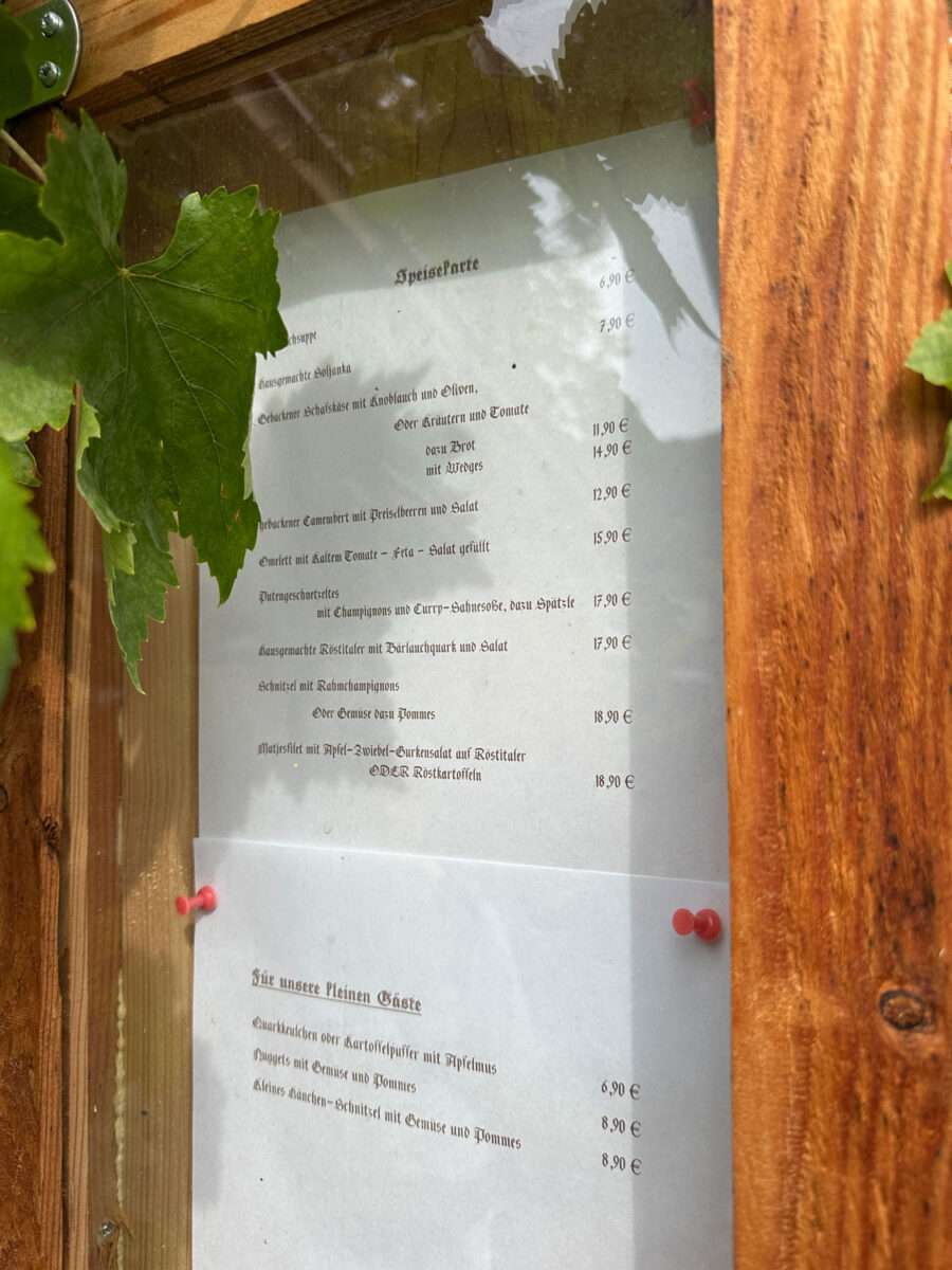 Ausgehängte Speisekarte des Gasthauses Zum frohen Mönch hinter einer Glasscheibe und Weinblättern