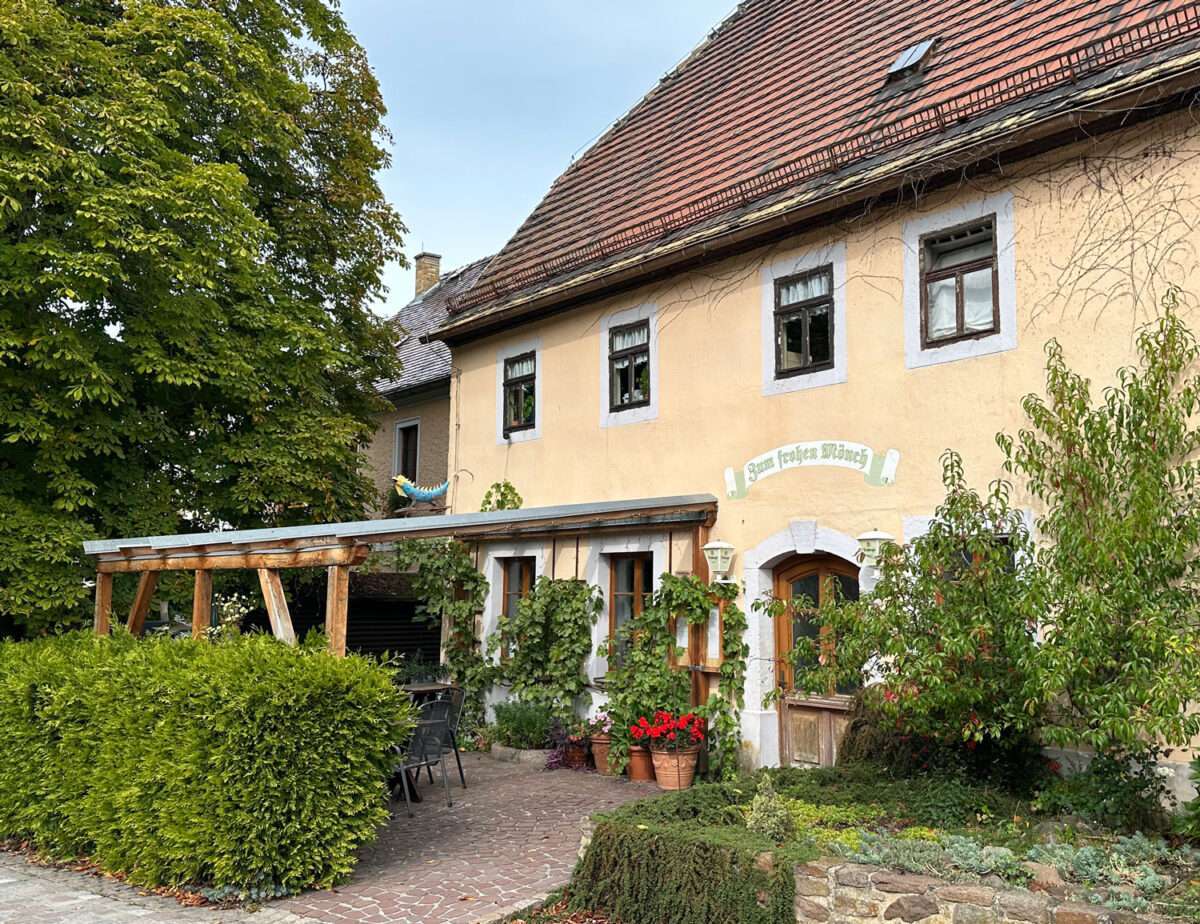 Begrüntes Gasthaus Zum frohen Mönch mit überdachten Sitzplätzen vor dem Eingang.