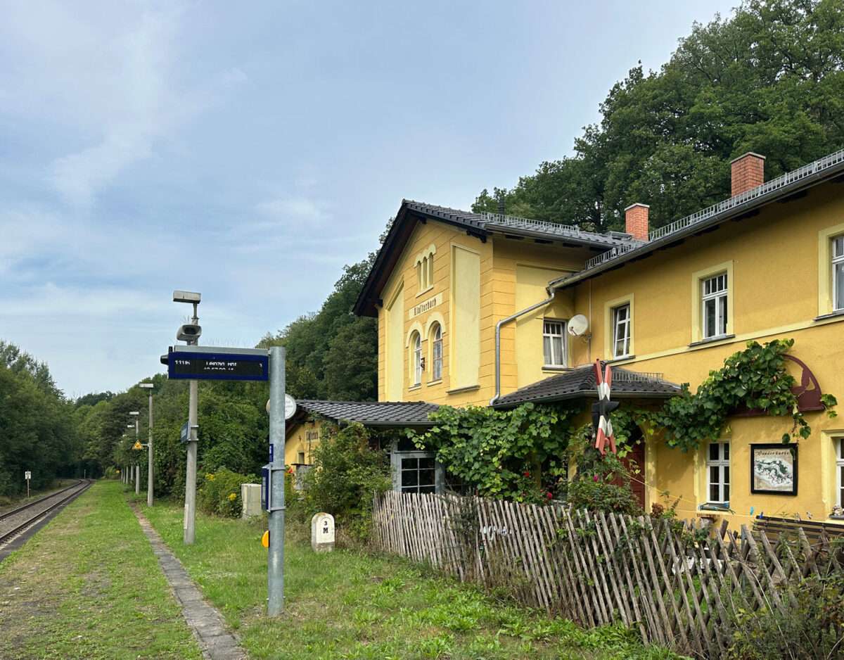 Gelbes Bahnhofsgebäude Klosterbuch neben dem Gleis und dem begrünten Bahnsteig