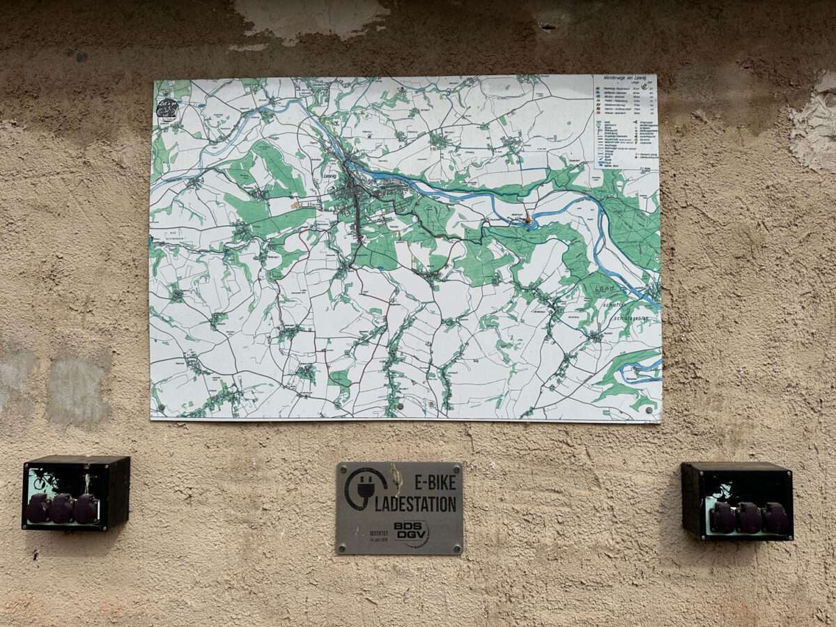 E-Bike-Ladestation mit Steckdosen und Wanderkarte an einer Hauswand im Kloster Buch
