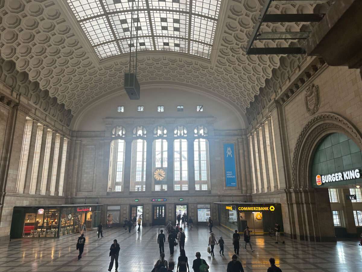 Große Halle des Leipziger Hauptbahnhofs mit gewölbter Kassettendecke, Glasdach, Uhr und Reisenden