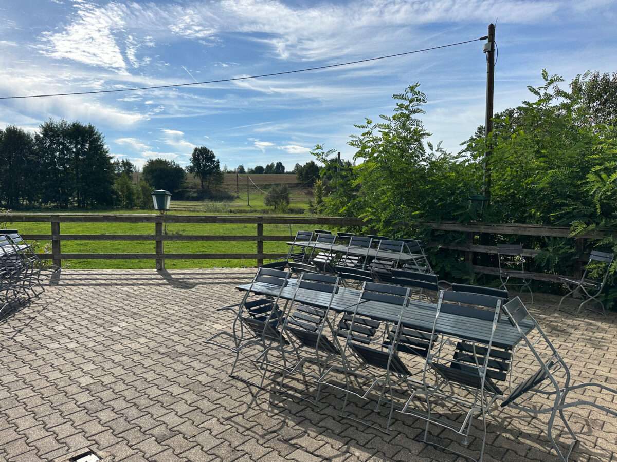 Gepflasterte Terrasse am Kanuheim Bischofswiese mit zusammengestellten Gartenstühlen und Blick über die Wiese.