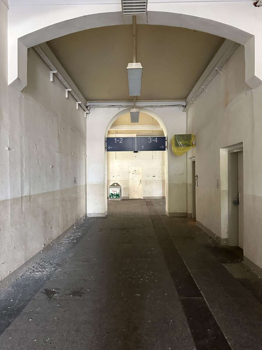Langer Durchgang im Döbelner Hauptbahnhof mit hohen Bögen, abgenutzten Wänden und einer geschlossenen Toilette.