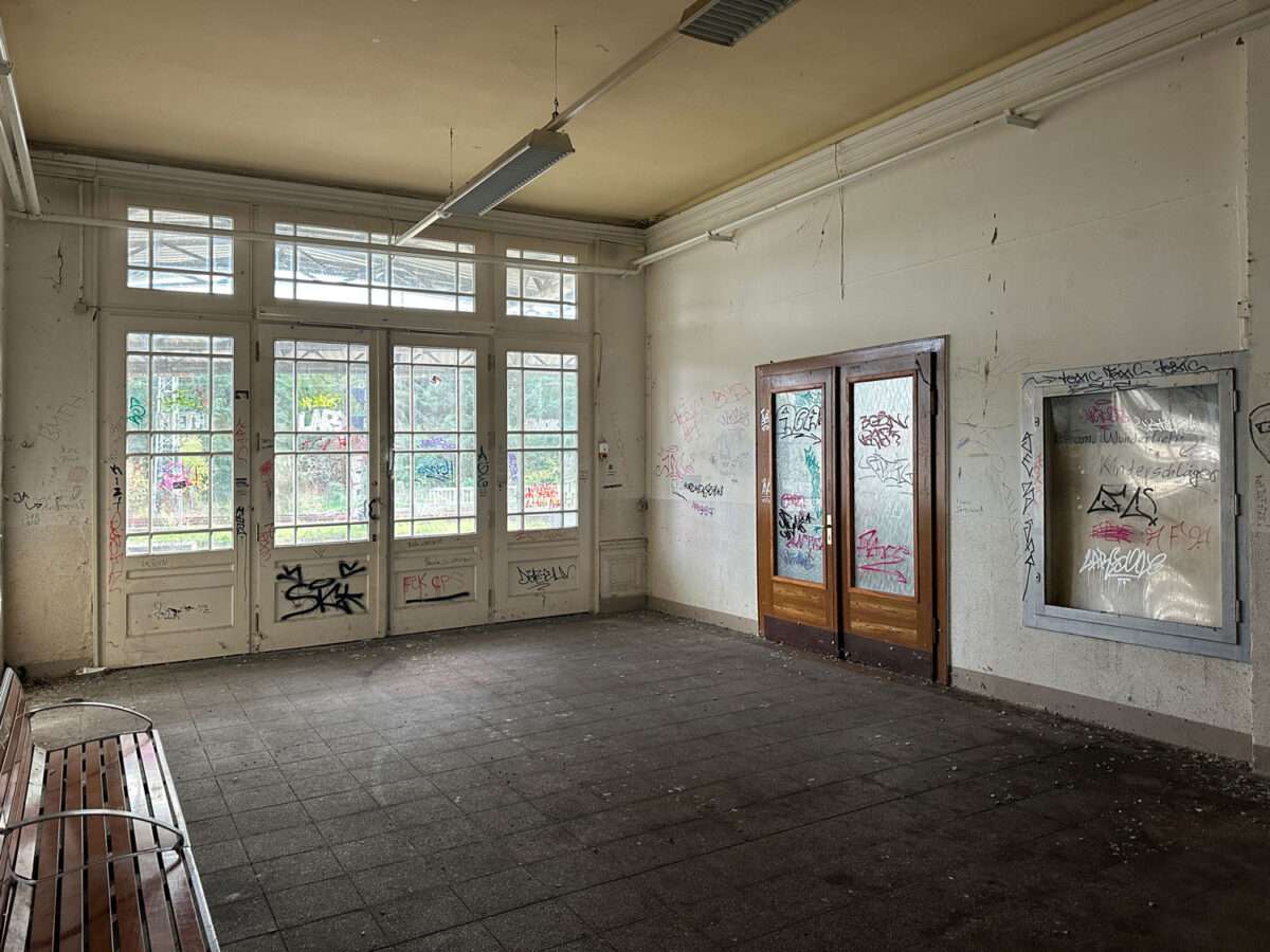Innenraum im Döbelner Hauptbahnhof mit verglasten Türen, Sitzbank links und verschmutzten, teilweise beschmierten Wänden.