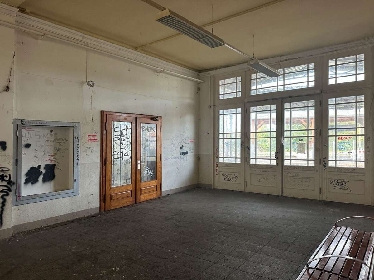Empfangsbereich im Döbelner Hauptbahnhof mit verglasten Türen, Sitzbank rechts und Graffiti an den Wänden.