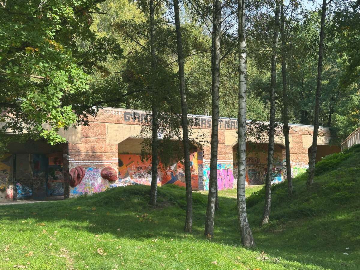 Ehemaliger Schießstand in den Döbelner Klosterwiesen mit offenen Backsteinbögen, bunten Graffiti und Kletterelementen hinter einer Baumreihe.