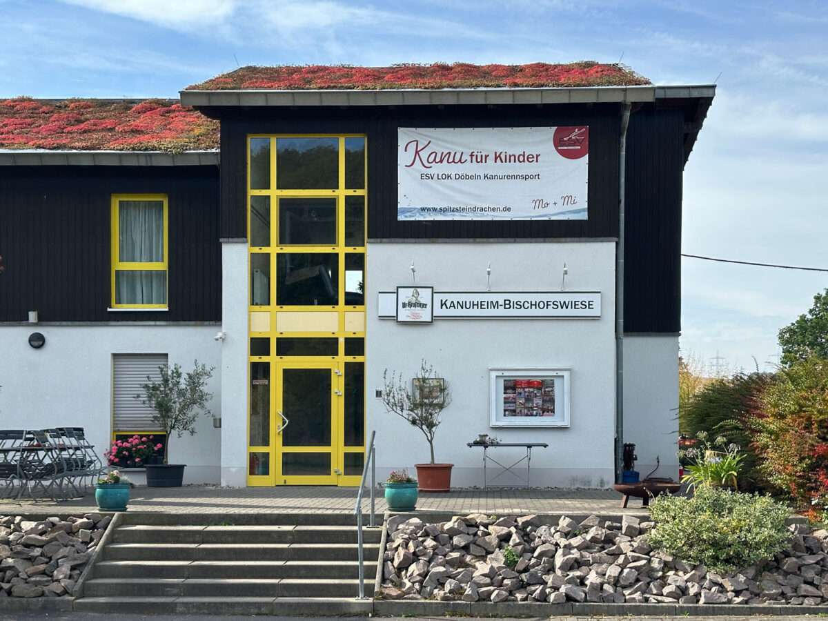 Kanuheim Bischofswiese bei Westewitz mit gelbem Glaseingang, vorgelagerter Treppe und einem Banner „Kanu für Kinder“.